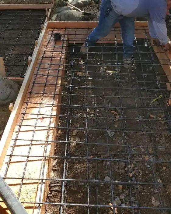 A worker tying a mat of reinforcing steel over gravel